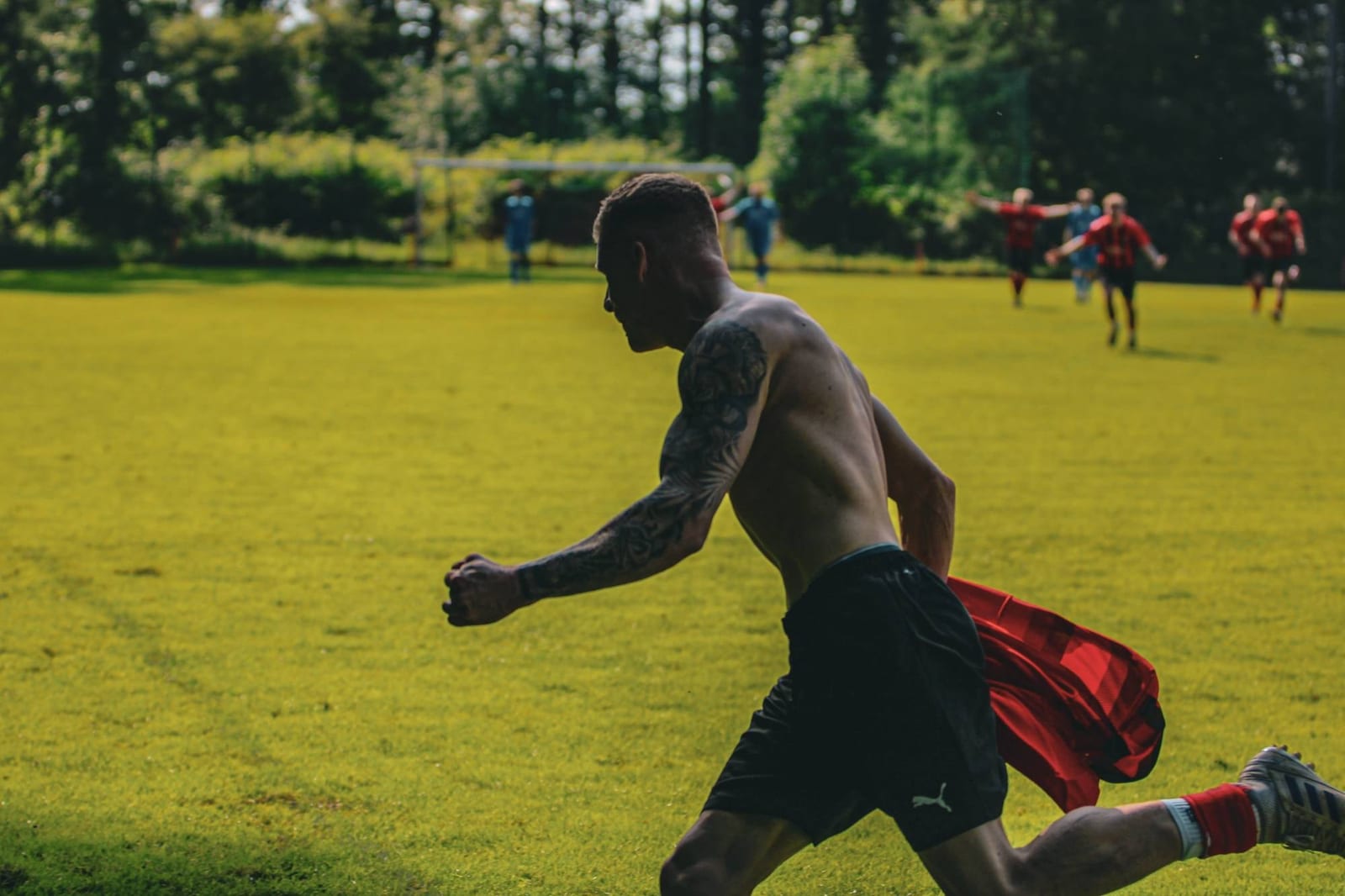 Nach dem Abpfiff rennt ein Spieler mit nacktem Oberkörper und dem Trikot in der Hand über den sonnigen Rasen