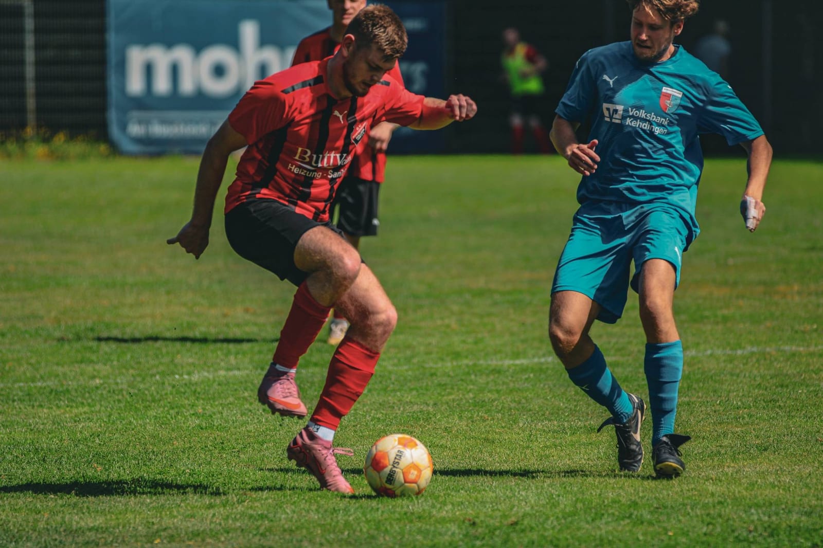 Spieler im rot-schwarz gestreiften Trikot führt den Ball, ein Gegenspieler in Türkis läuft an