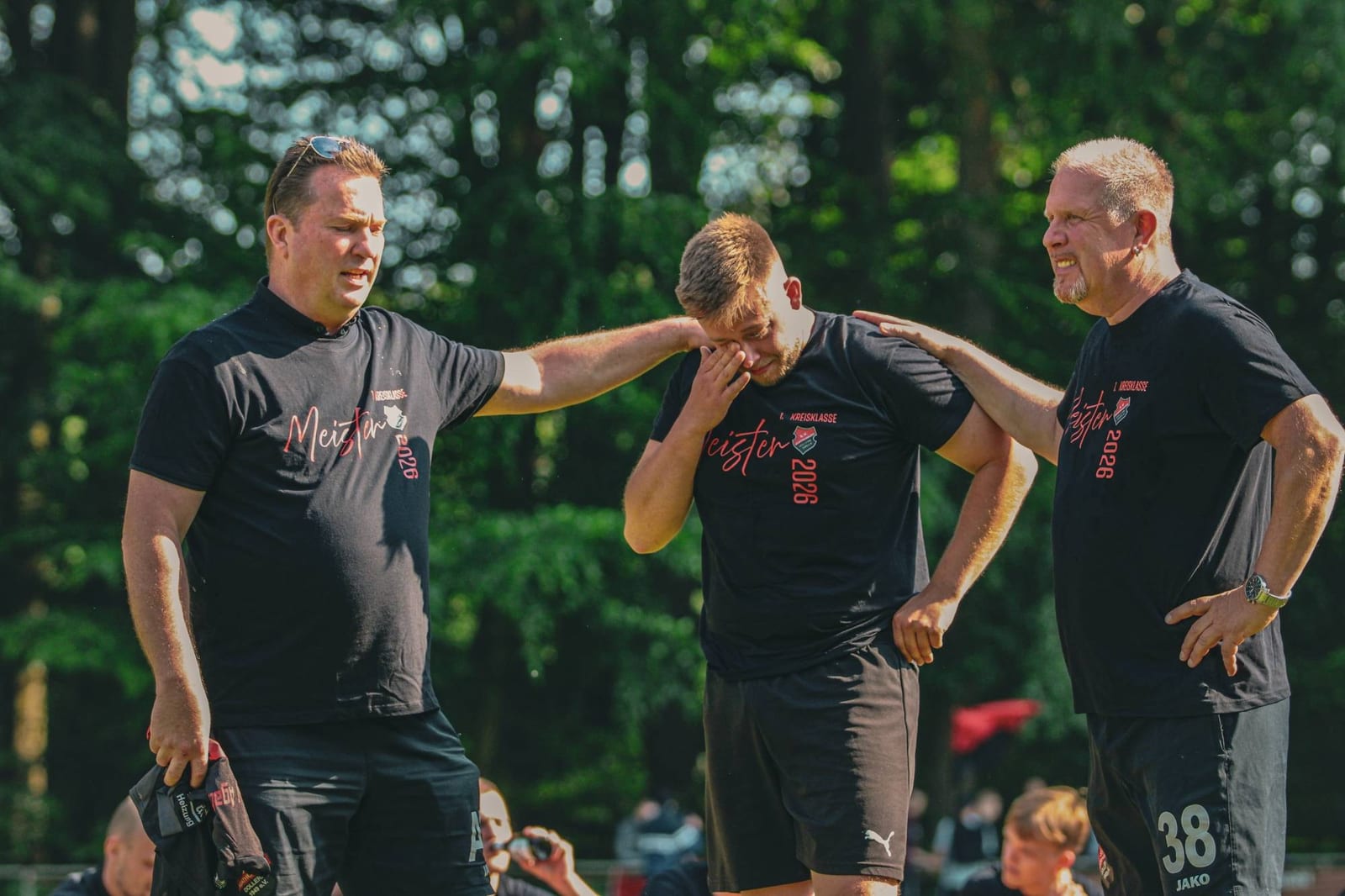 Zwei Männer im Meister-Shirt legen einem Spieler die Hände auf die Schultern, er wischt sich übers Gesicht