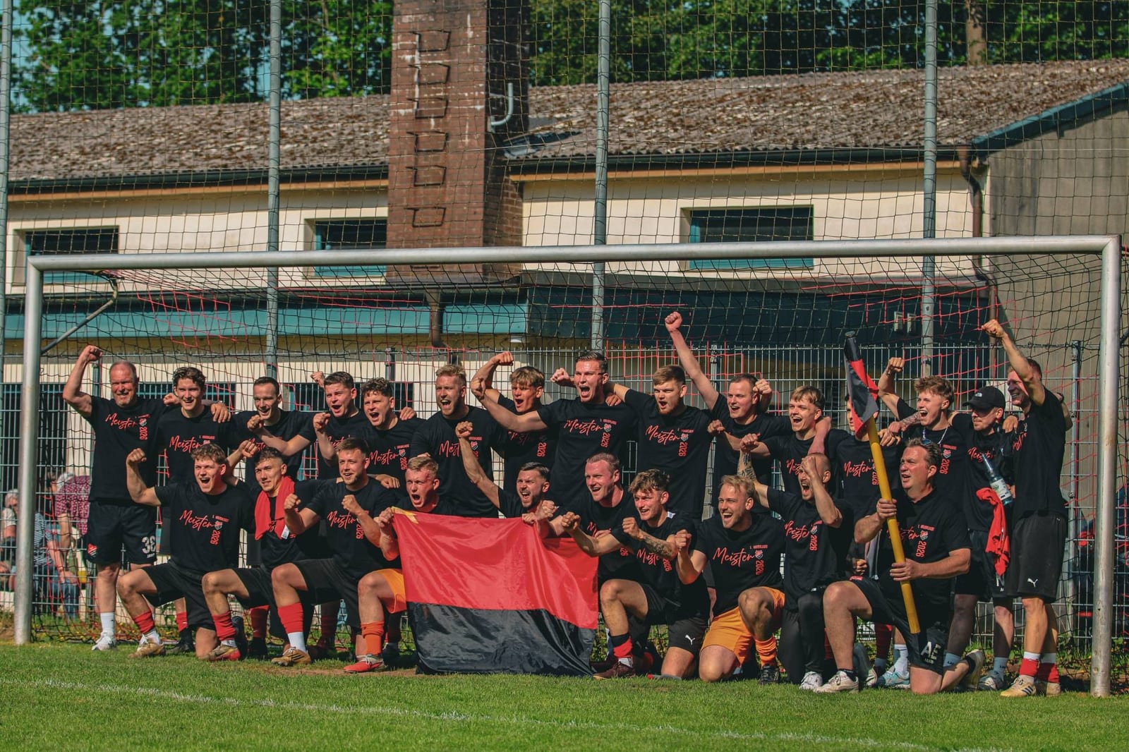 Mannschaftsfoto vor dem Tor in schwarzen Meister-Shirts mit rot-schwarzer Fahne