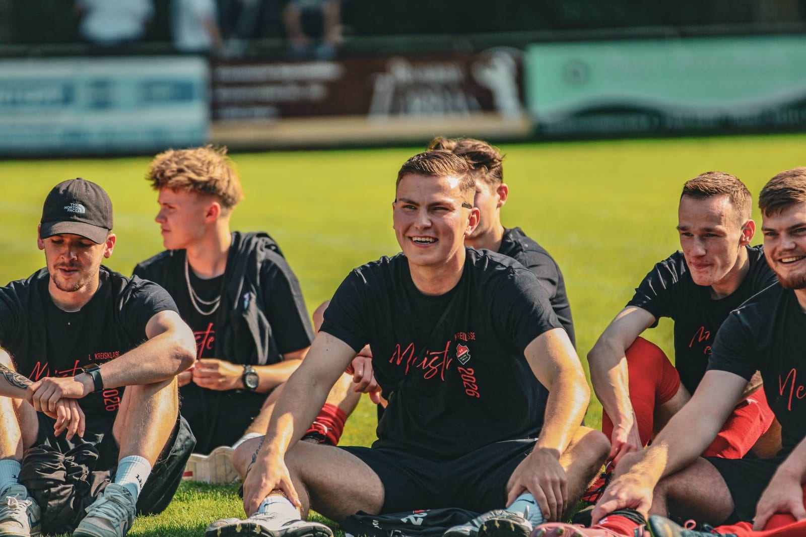 Spieler in Meister-Shirts sitzen lachend nebeneinander im Gras