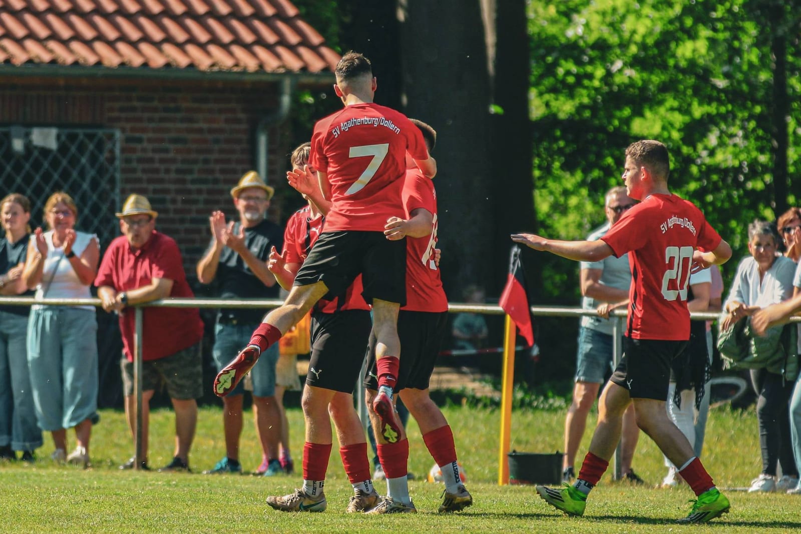 Torjubel vor der Bande: Ein Spieler mit der Nummer 7 springt einem Mitspieler entgegen, Zuschauer klatschen
