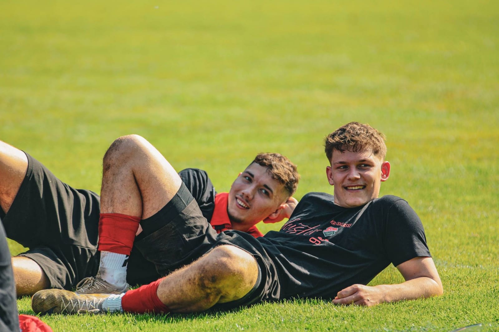 Zwei Spieler liegen lachend nebeneinander im Gras