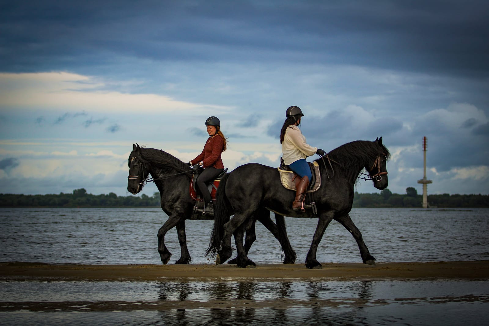 Zwei Reiterinnen reiten im Schritt hintereinander über den nassen Elbstrand