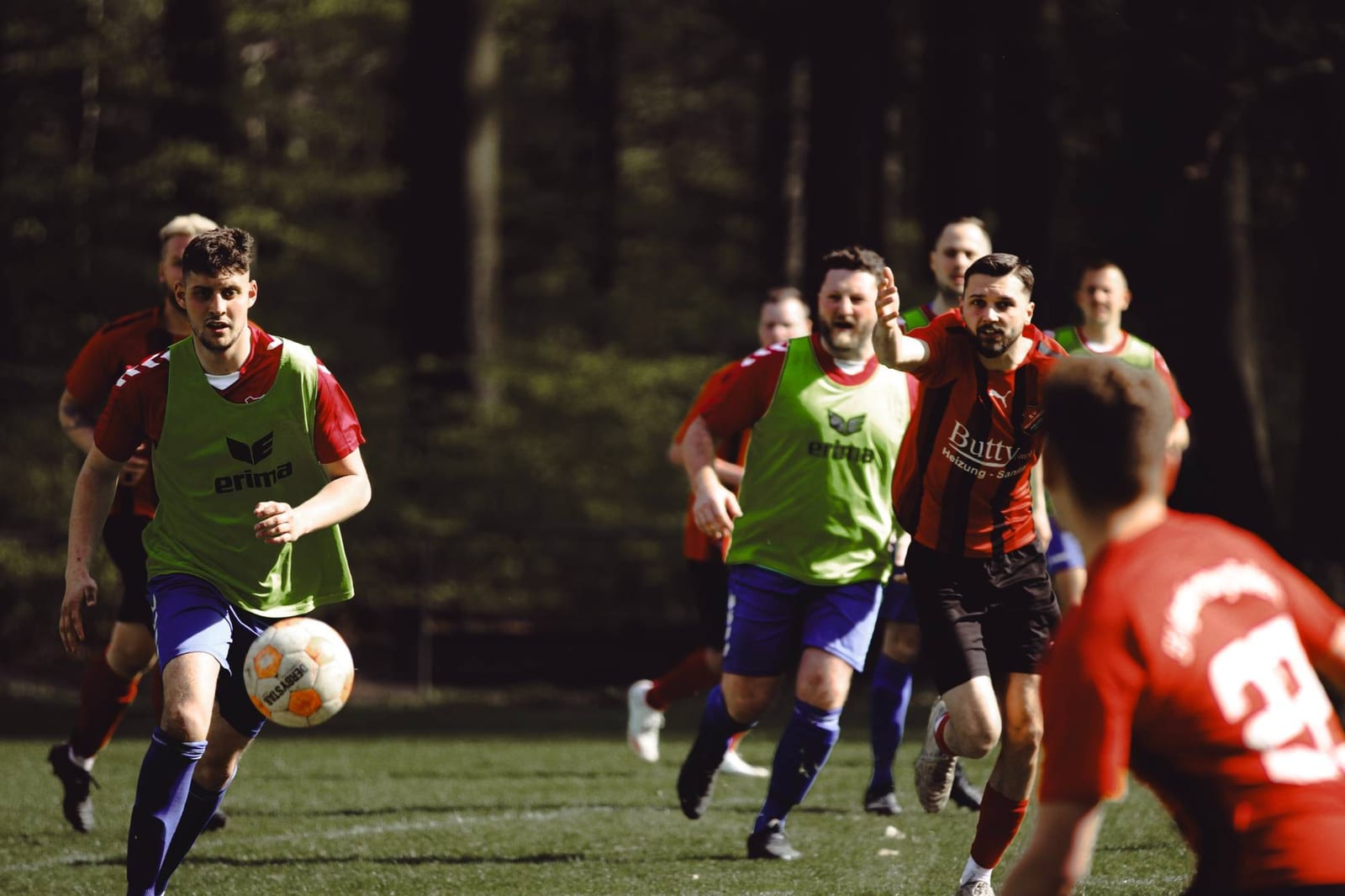 Ein Spieler im grünen Überzieher führt den Ball nach vorn, mehrere Spieler laufen mit