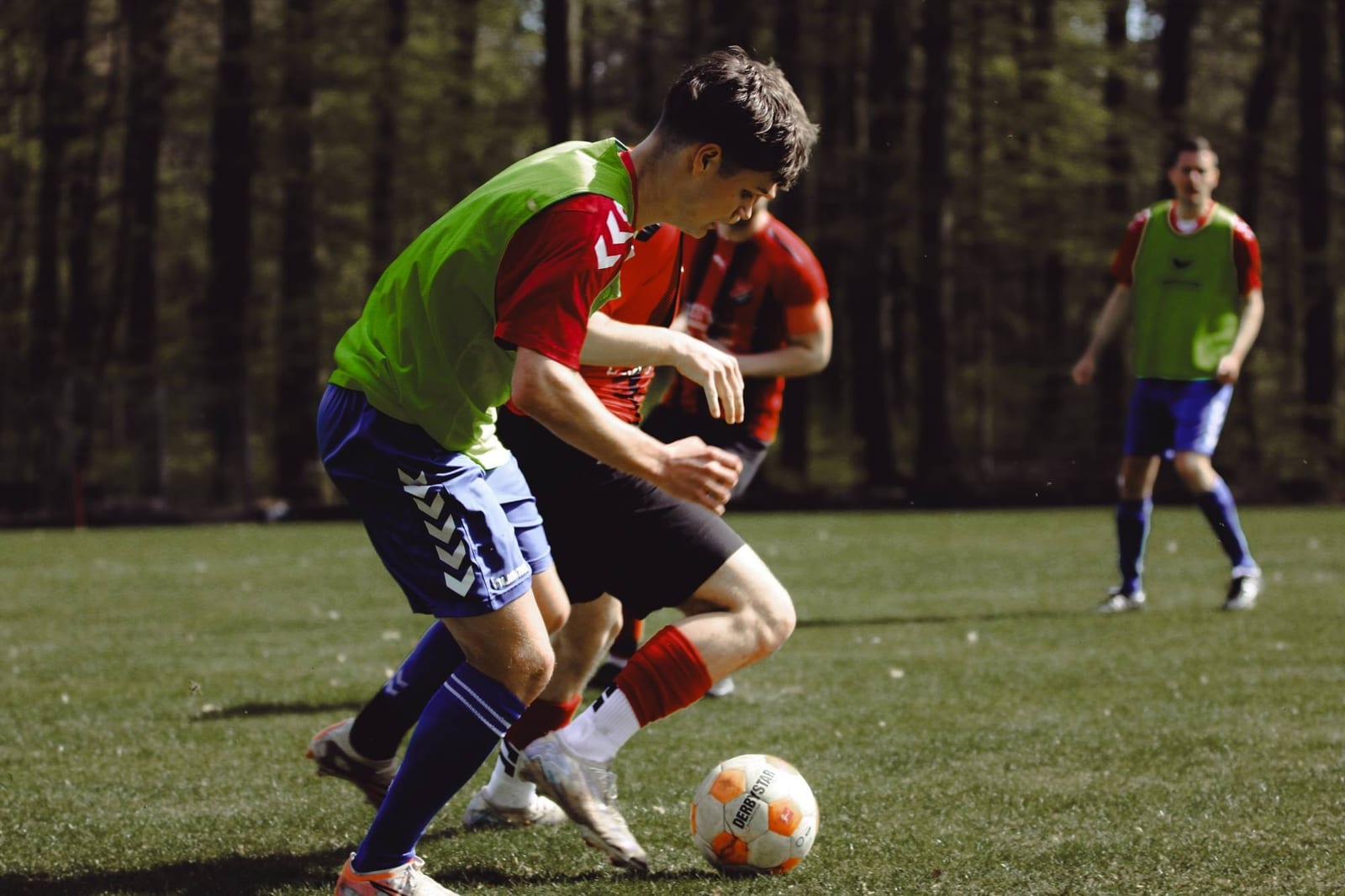 Ein Spieler im grünen Überzieher und ein Spieler in Rot kämpfen eng um den Ball