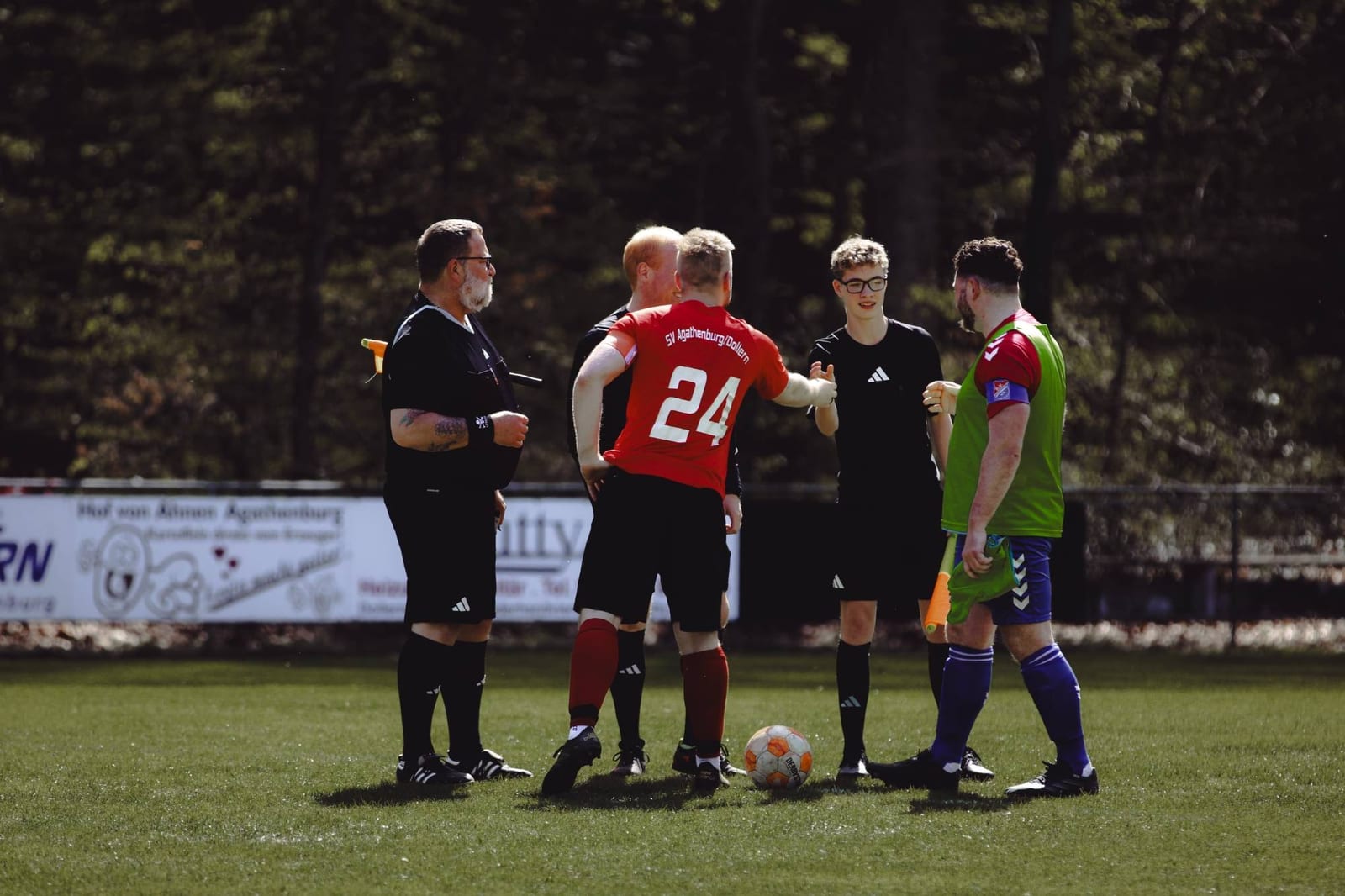 Spieler beider Mannschaften diskutieren mit dem Schiedsrichter, der Ball liegt am Boden
