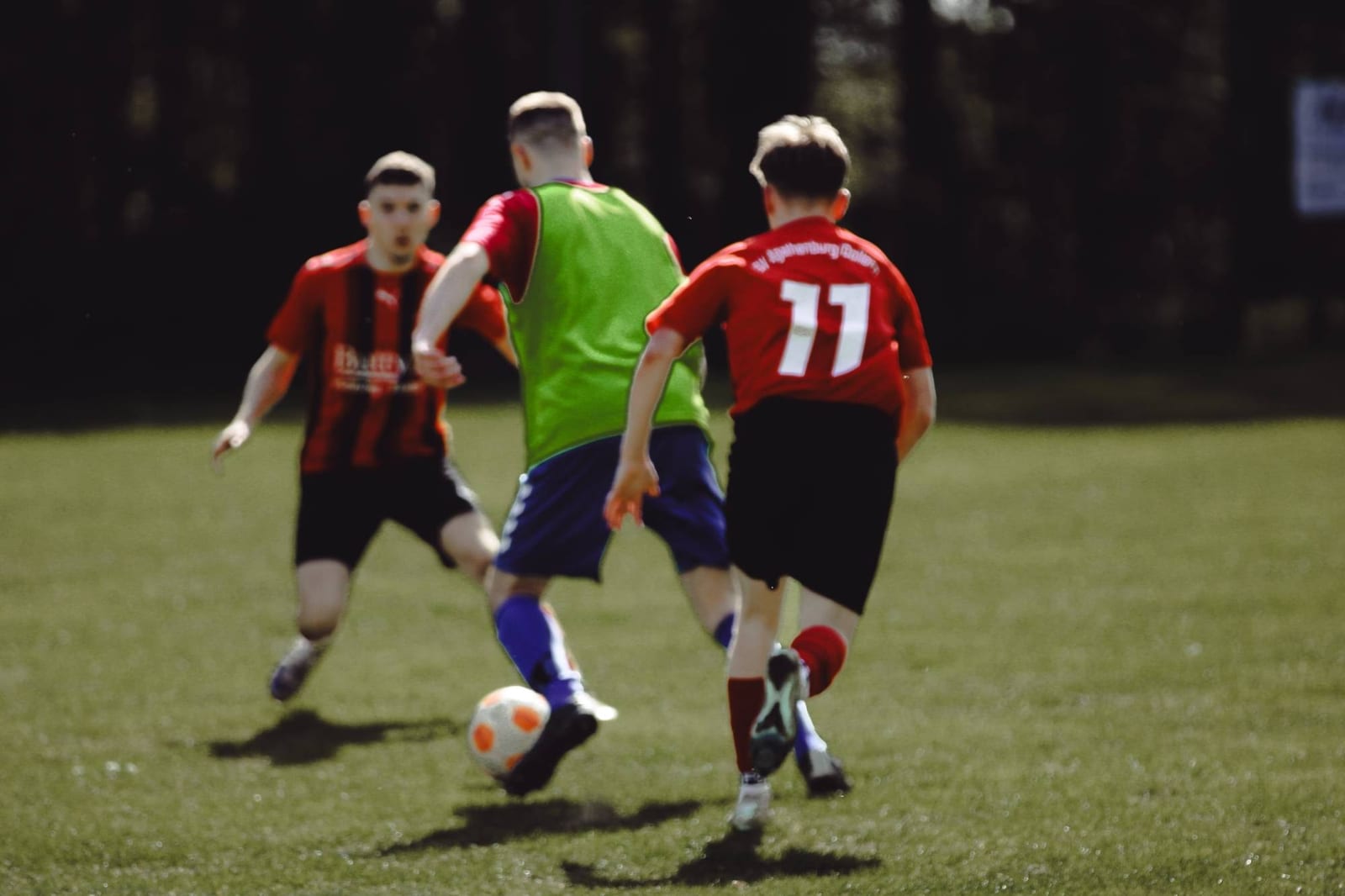 Spieler mit der Nummer 11 dribbelt zwischen zwei Gegenspielern