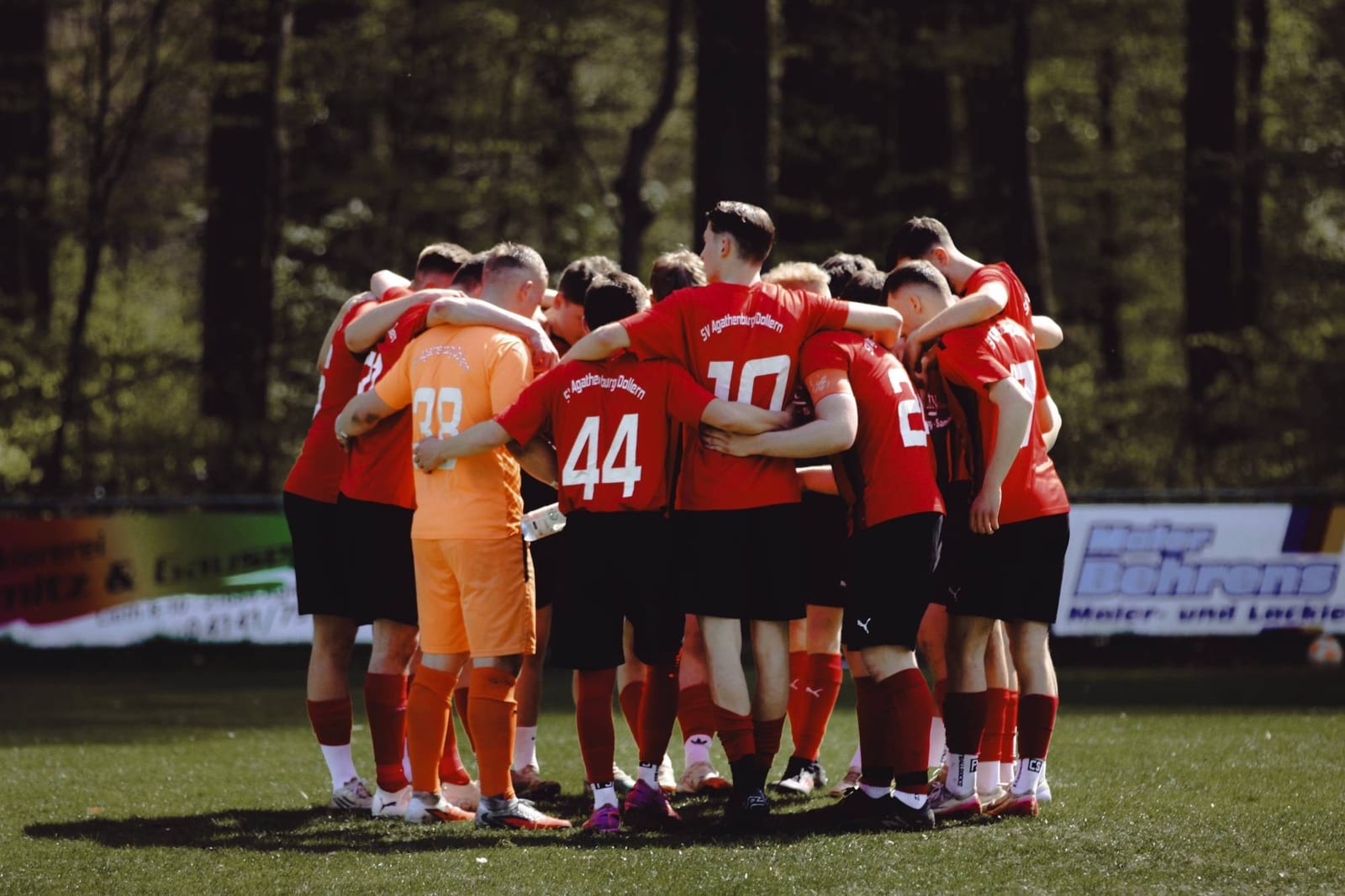 Mannschaft in Rot steht vor dem Anpfiff im Kreis, in der Mitte der Torwart in Orange
