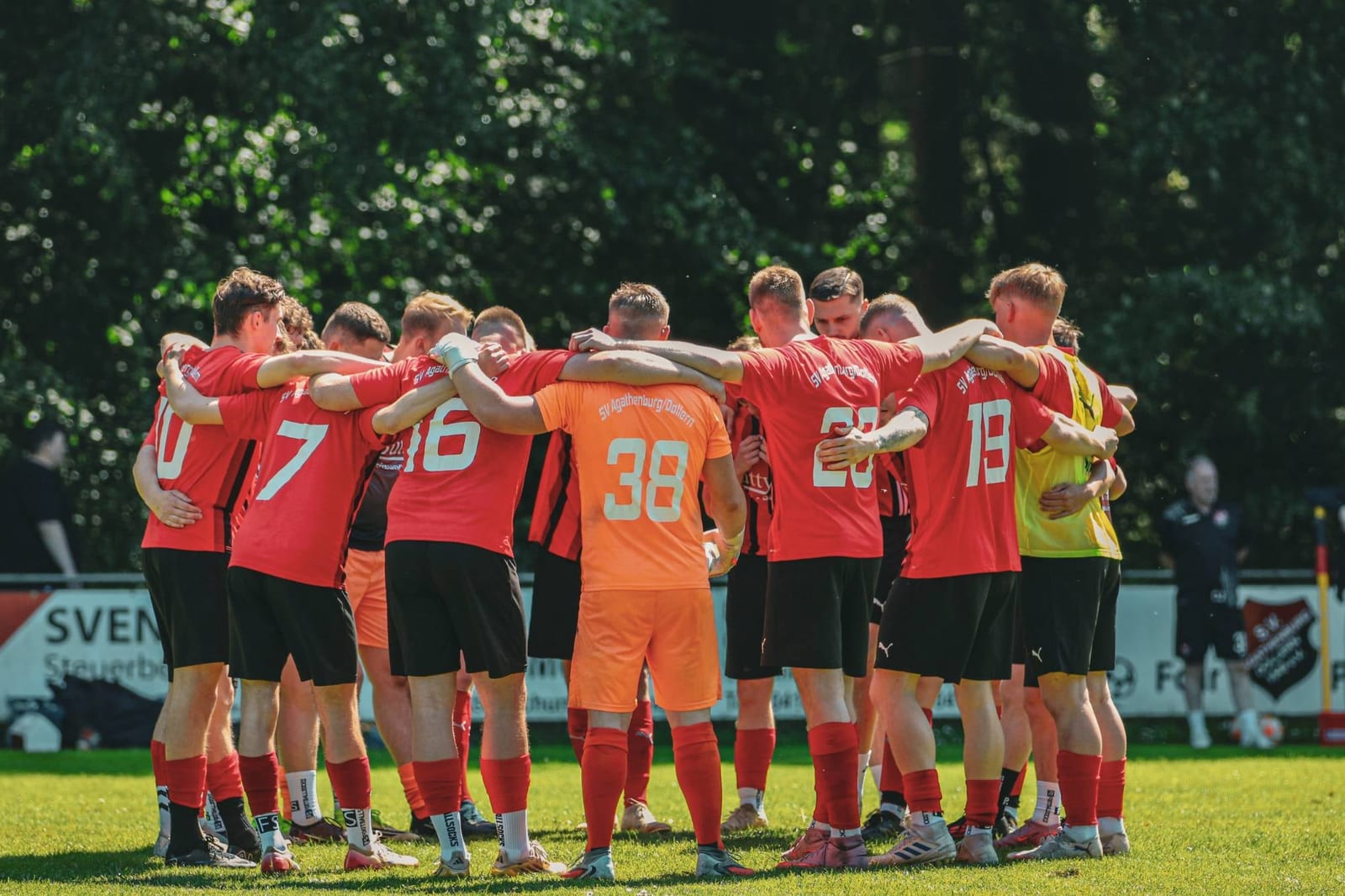 Mannschaft in Rot mit Torwart in Orange steht vor dem Anpfiff im Kreis