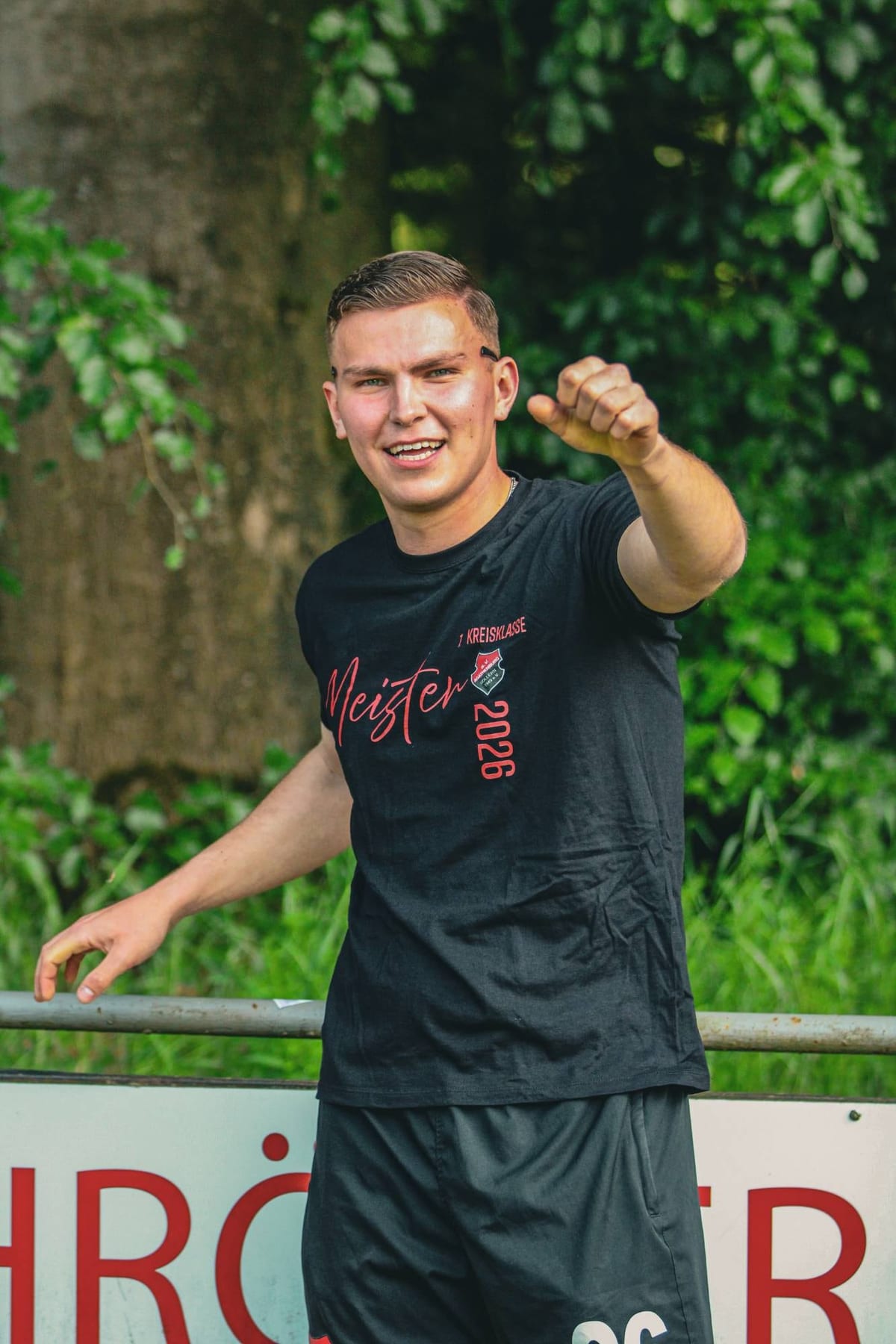 Spieler im schwarzen Meister-Shirt 2026 zeigt lachend in die Kamera