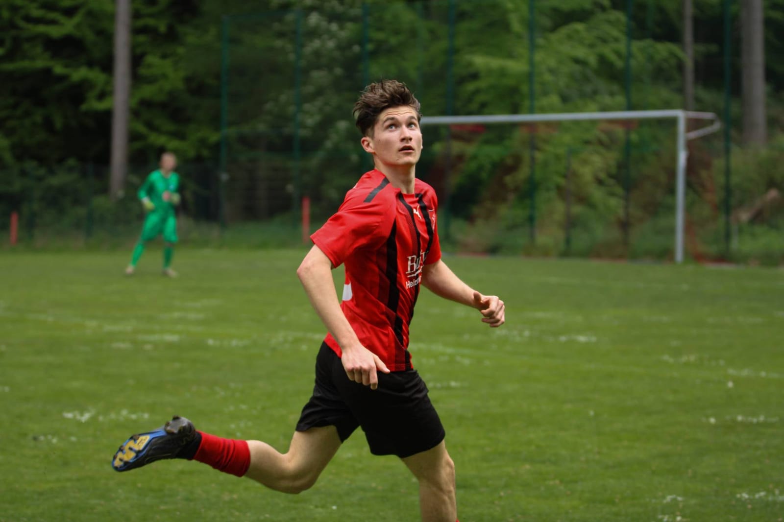 Spieler im rot-schwarz gestreiften Trikot sprintet mit Blick zum Ball über den Platz
