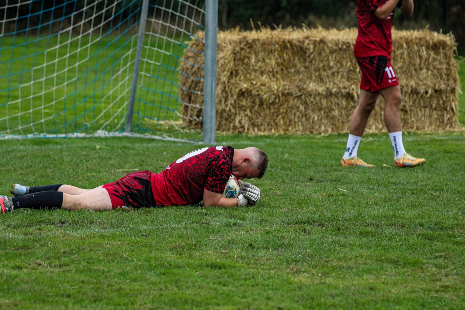 Torwart liegt nach der Parade im Gras und hält den Ball fest