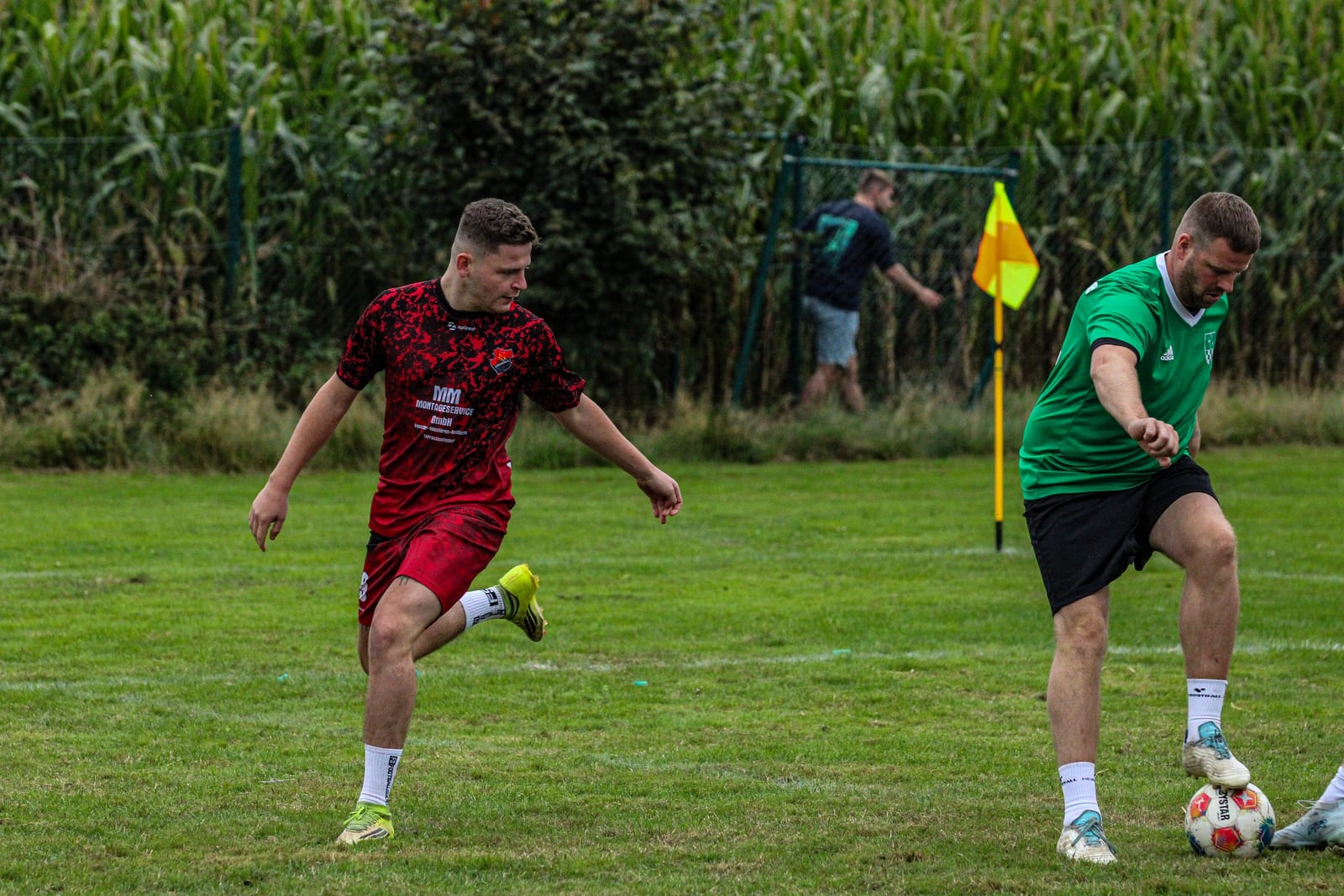 Zweikampf um den Ball nahe der Eckfahne, rotes gegen grünes Trikot