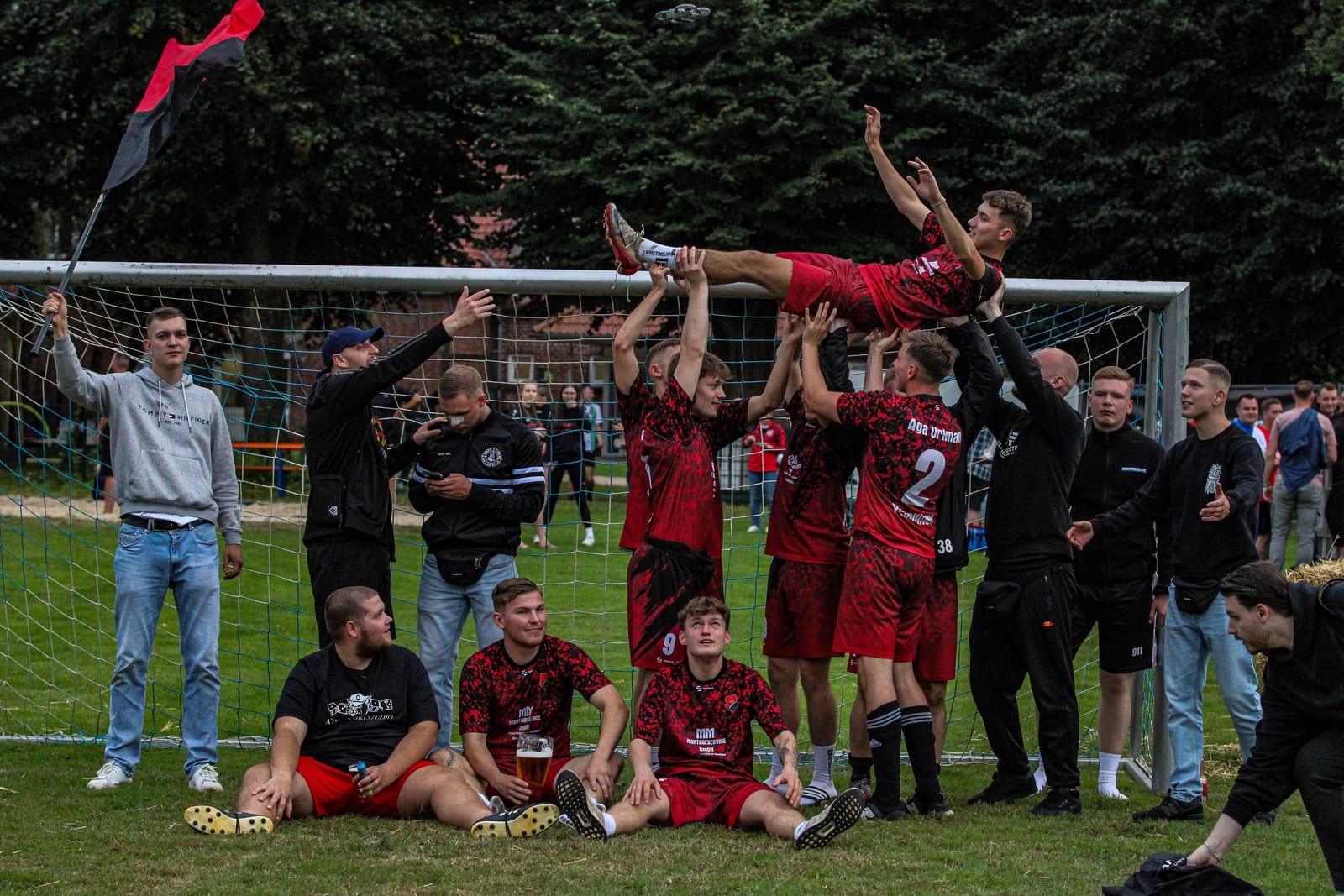 Beim Mannschaftsfoto vor dem Tor werfen die Spieler einen Mitspieler in die Luft, links weht eine rot-schwarze Fahne