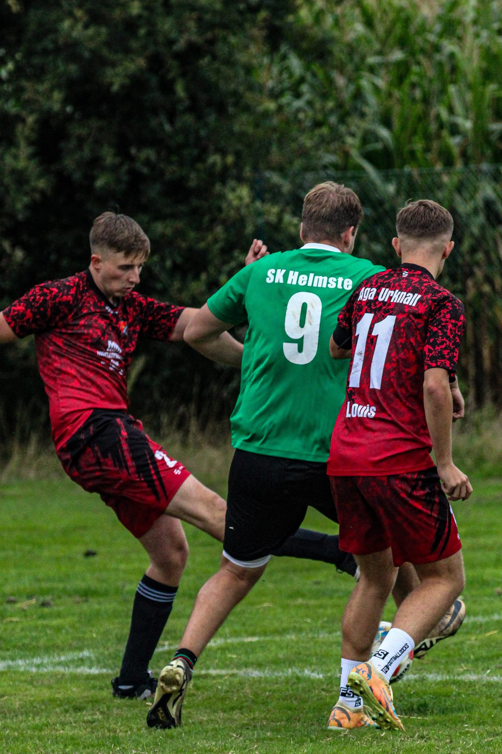 Ein Spieler in Rot schießt, ein Gegenspieler im grünen Trikot mit der Nummer 9 versucht zu blocken
